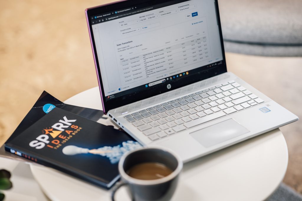 Laptop, coffee, and notebook on table.